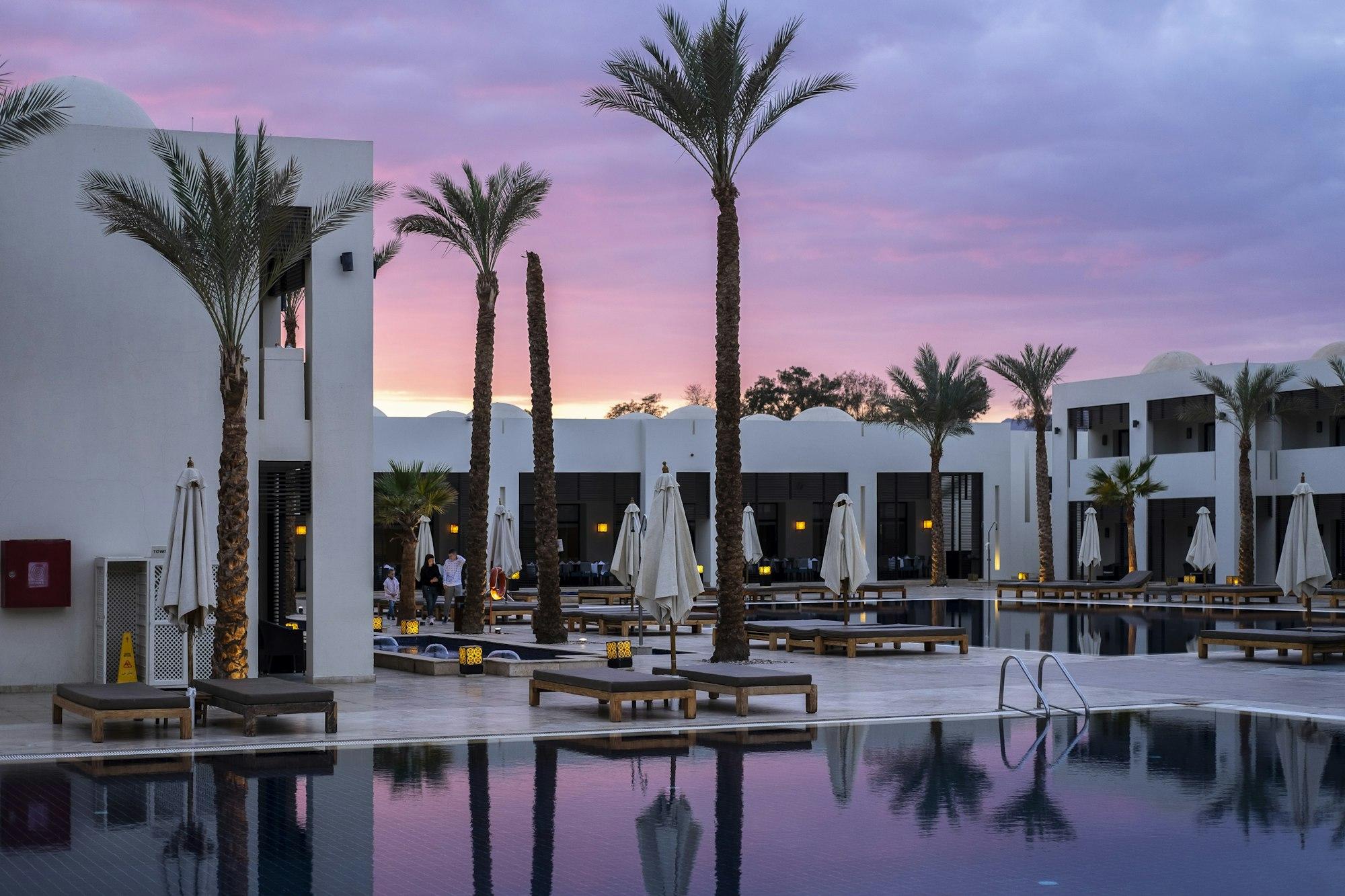 A lit resort pool lined with palm trees at dusk